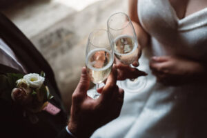 Close up of married couple toasting champagne glasses at wedding party. Hands bride and groom clinking glasses at wedding reception.
